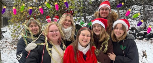 Styrelsen 2025, Melina Lindholm, Noomi Talvio, Sofie Lehtovaara, Emilia Melén, Jennifer Lindgren, Niko Sandberg och Svea Välimäki klädda i tomteluvor och juldekorationer