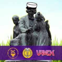 Topeliusstatyn på gräsmattan, statyn har en examensmössa på sig. I den nedre delen av bilden en mörklila balk och ÅAS, VYYs och VAMOKs logon