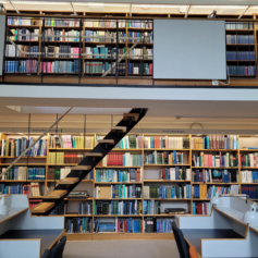 Foto från biblioteket Boktornet: Arbetsstationer, bokhyllor fulla med böcker och trappor som går upp till andra våningen där det också finns hyllvis med böcker